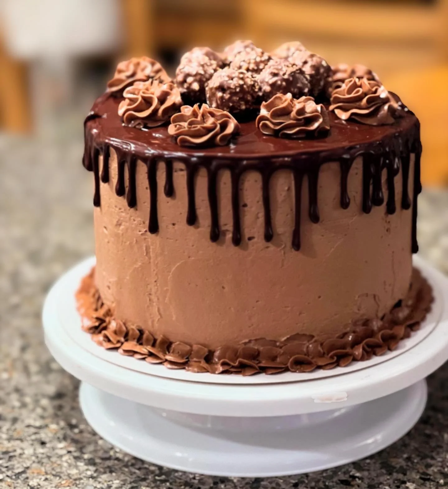 Chocolate cake with chocolate frosting, drizzled with chocolate ganache, topped with chocolate truffles and piped chocolate decorations, on a white cake stand.