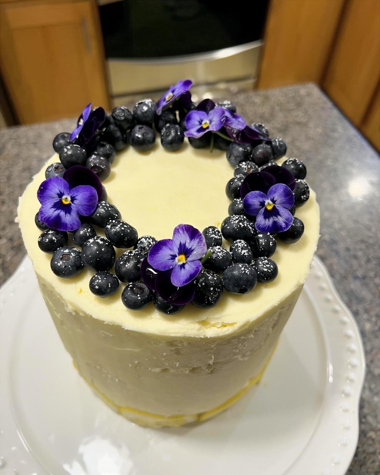A tall cake decorated with purple and white edible flowers and blackberries on top.