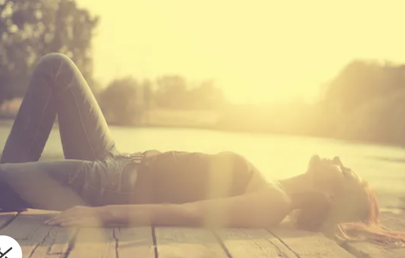 Women relaxing on a wooden dock during sunset, with the sun low in the sky and trees in the background.