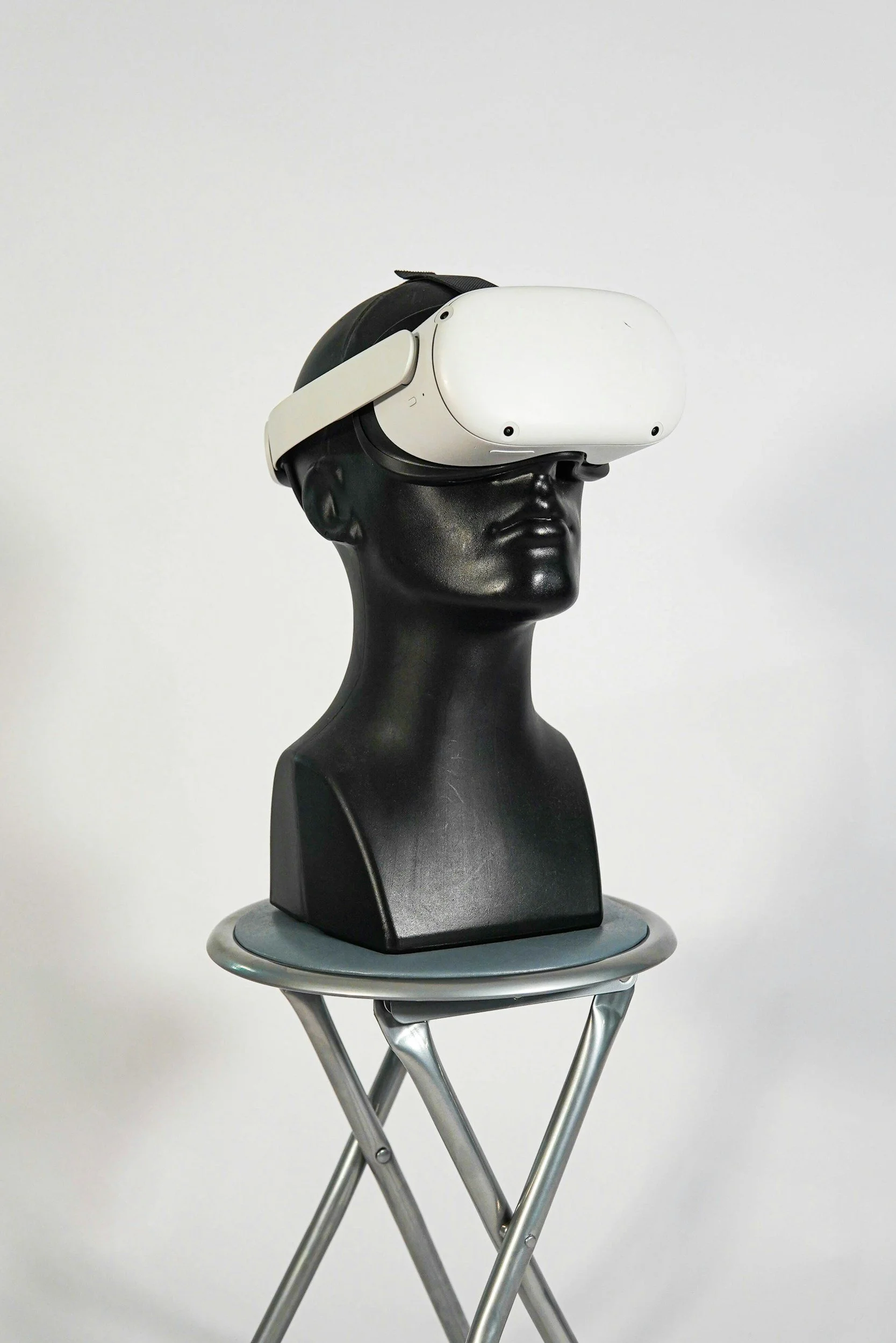 Black mannequin head with a white virtual reality headset on, placed on a small metallic table with a folding design.
