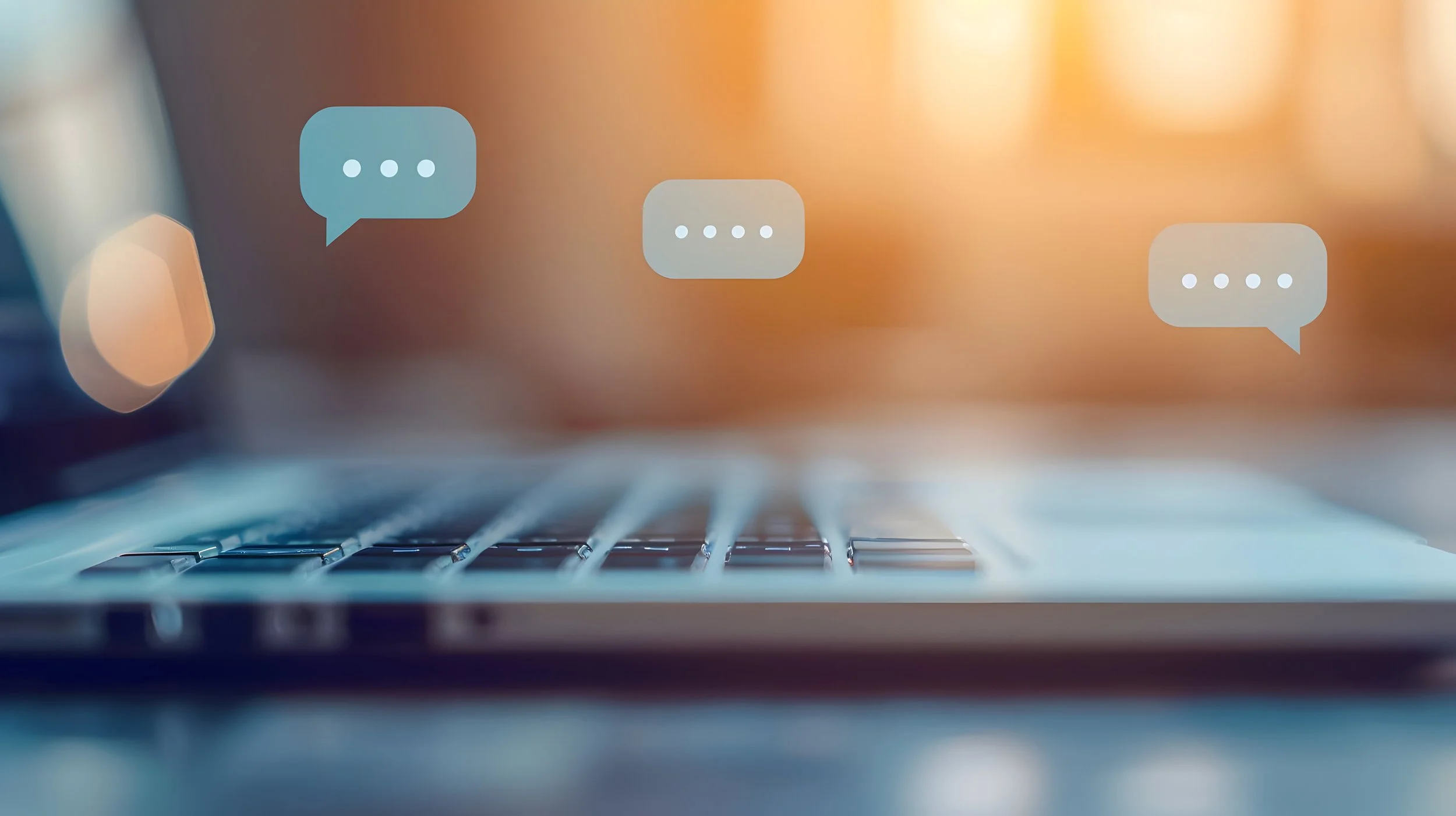 A laptop keyboard with three speech bubble icons indicating digital messaging or chat conversations floating above.