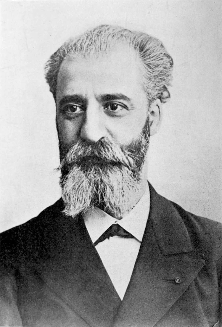 Black and white portrait of a man with a beard and mustache, wearing a suit and tie, looking to the side.