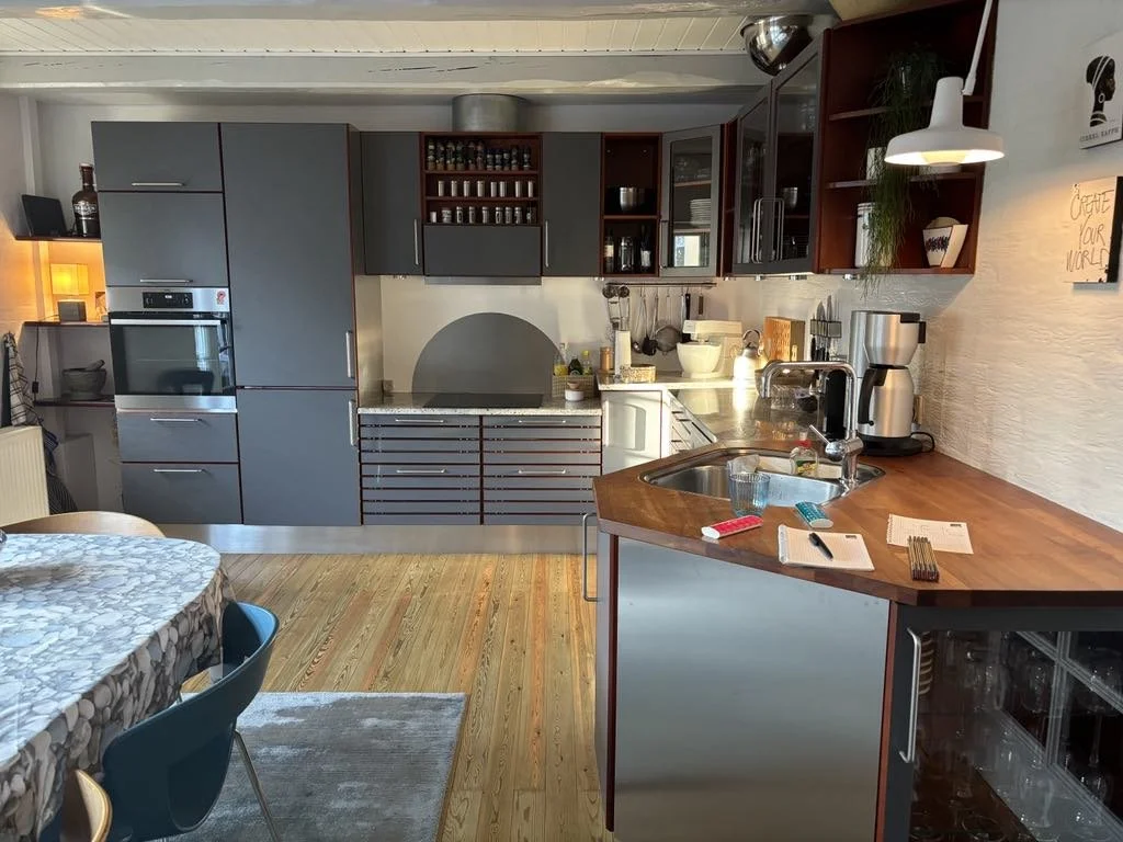 Modern kitchen with gray cabinets, wooden countertops, and a small dining table with a patterned tablecloth.