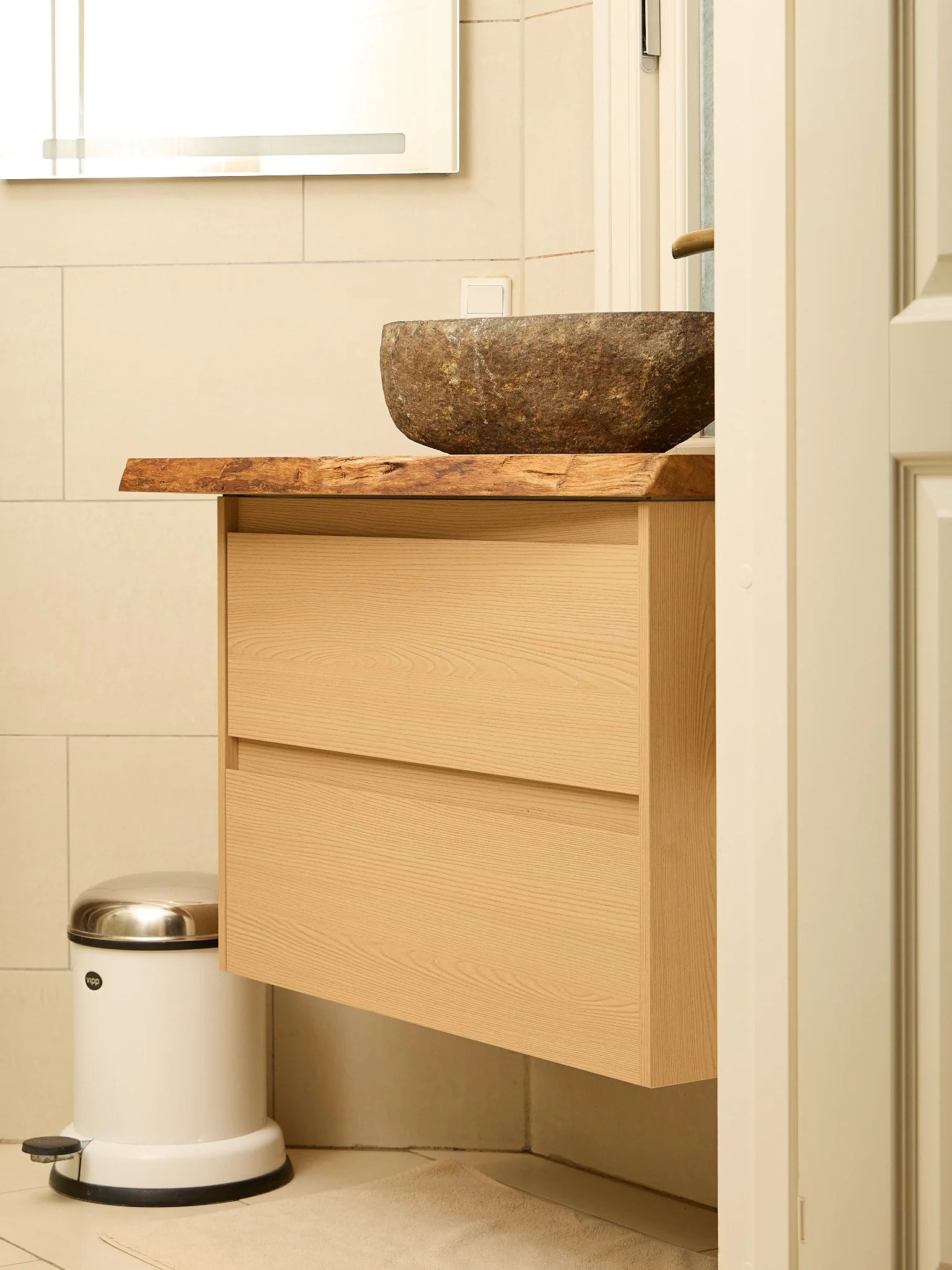 A bathroom with a stone sink on a wooden countertop, a small trash can, and a radiator.