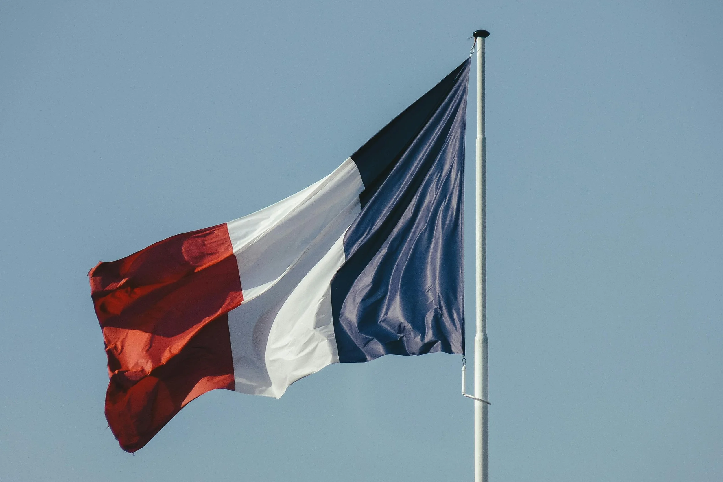 Drapeau français flottant au vent contre un ciel clair.