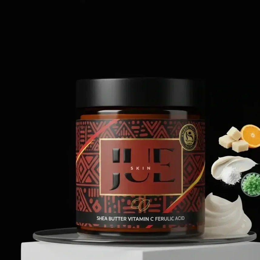 A jar of skincare cream labeled 'Shea Butter Vitamin C Ferulic Acid' by Jueskin on a white platform with ingredients like shea butter, vitamin C, lemon, and green granules next to it, against a black background.