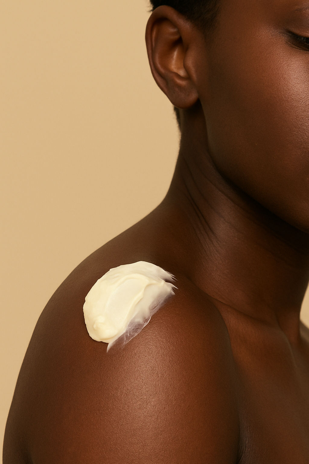 Close-up of a woman with dark skin applying white cream or moisturizer on her shoulder.