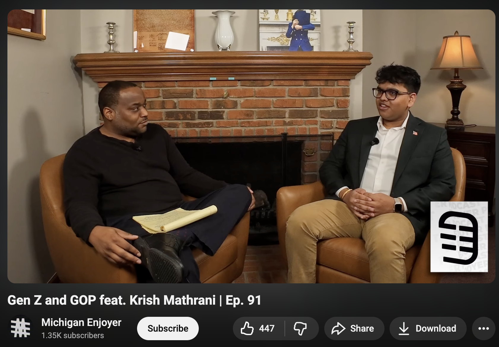 Two men seated and talking in a room with a brick fireplace, with a framed photo, a white vase, and decorative items on the mantel. One man wears a black shirt, the other a suit and glasses. They are having a conversation on young voters in Michigan.