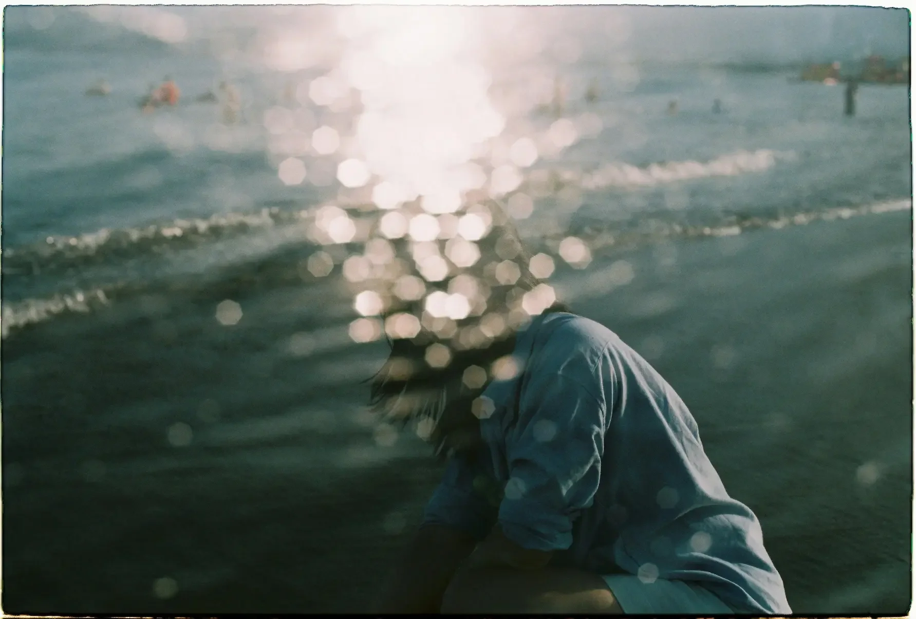 A person sitting quietly by the water as light reflects across the surface.
