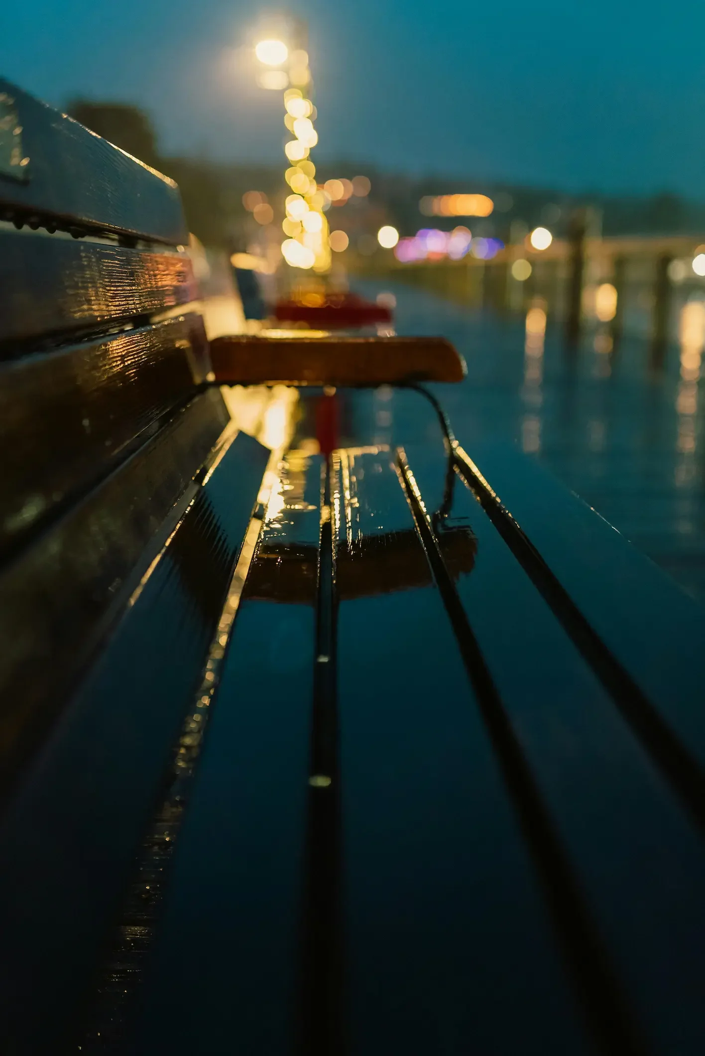 An empty park bench at night after rain, reflecting city lights in a quiet urban setting