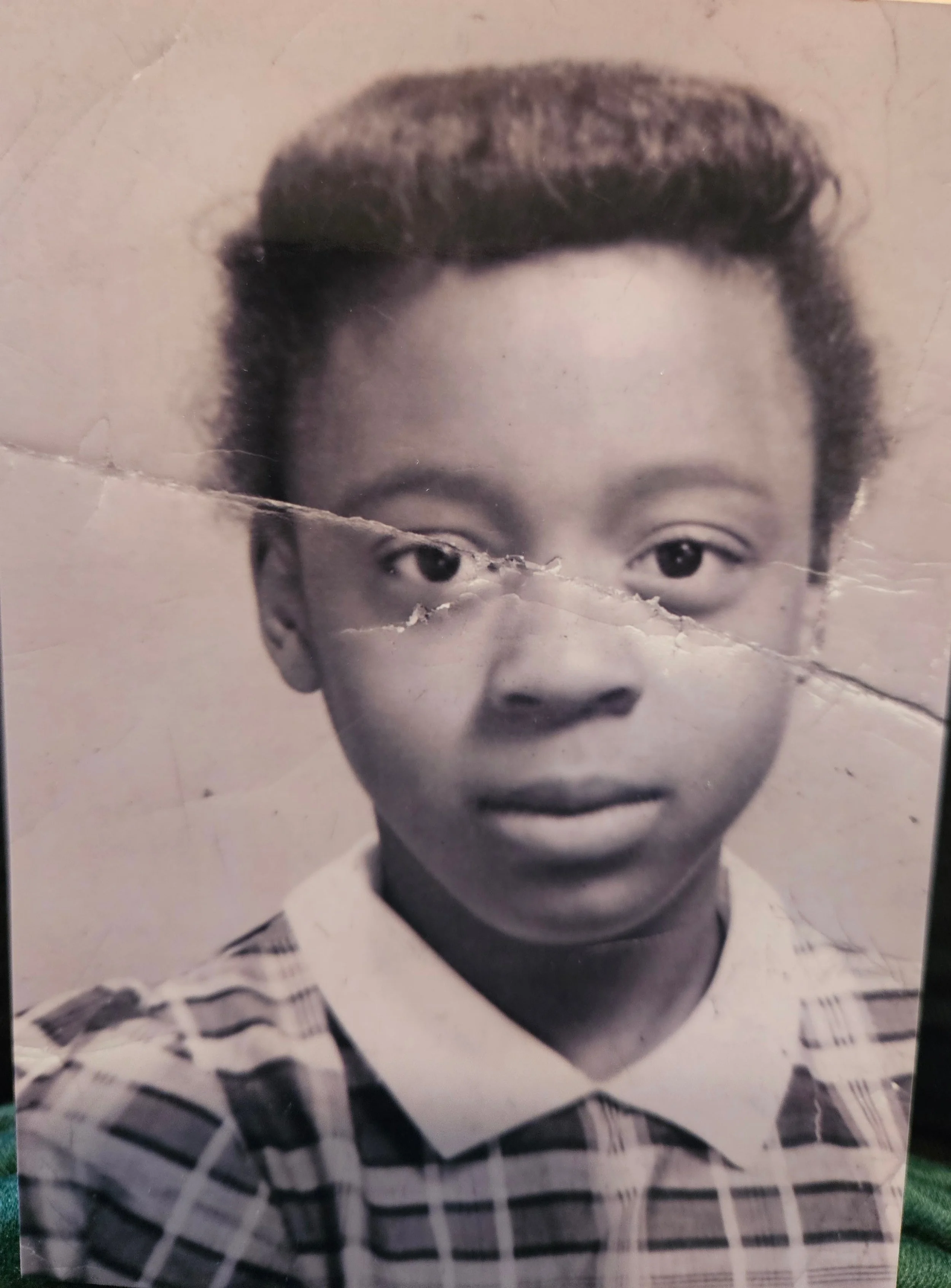 Black-and-white photo of a young boy with short hair, wearing a collared, checkered shirt.