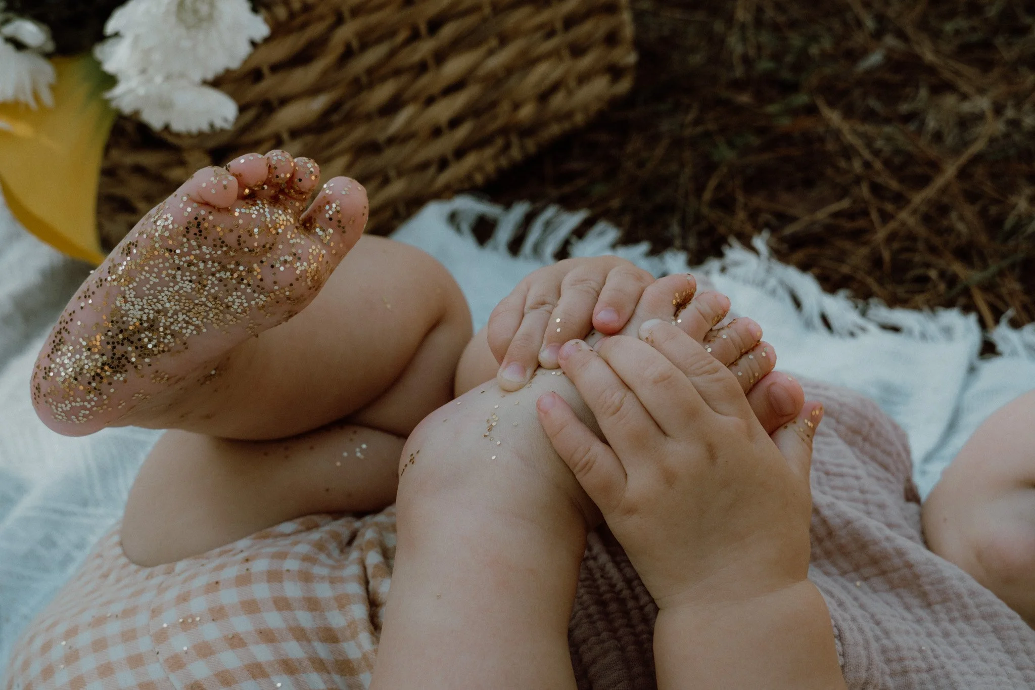 Children's hands covered in glitter touching in a circle, with a wicker basket and a yellow object in the background.