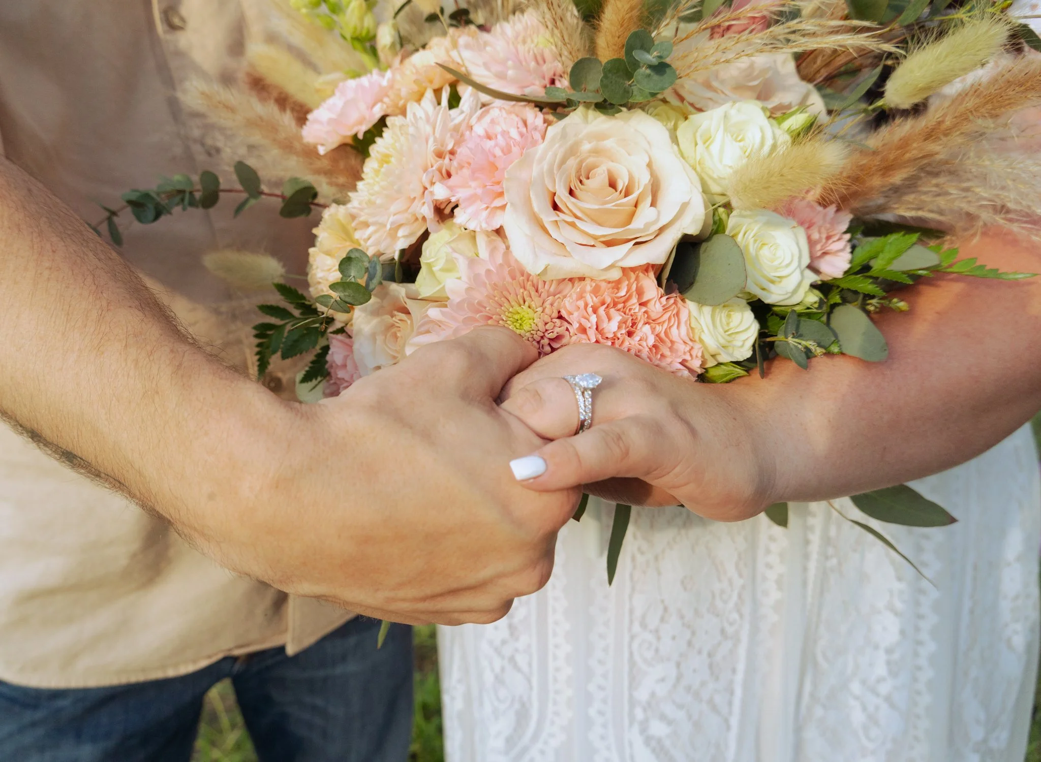 Person holding a bouquet of pink, white, and cream flowers with greenery and dried grass accents.