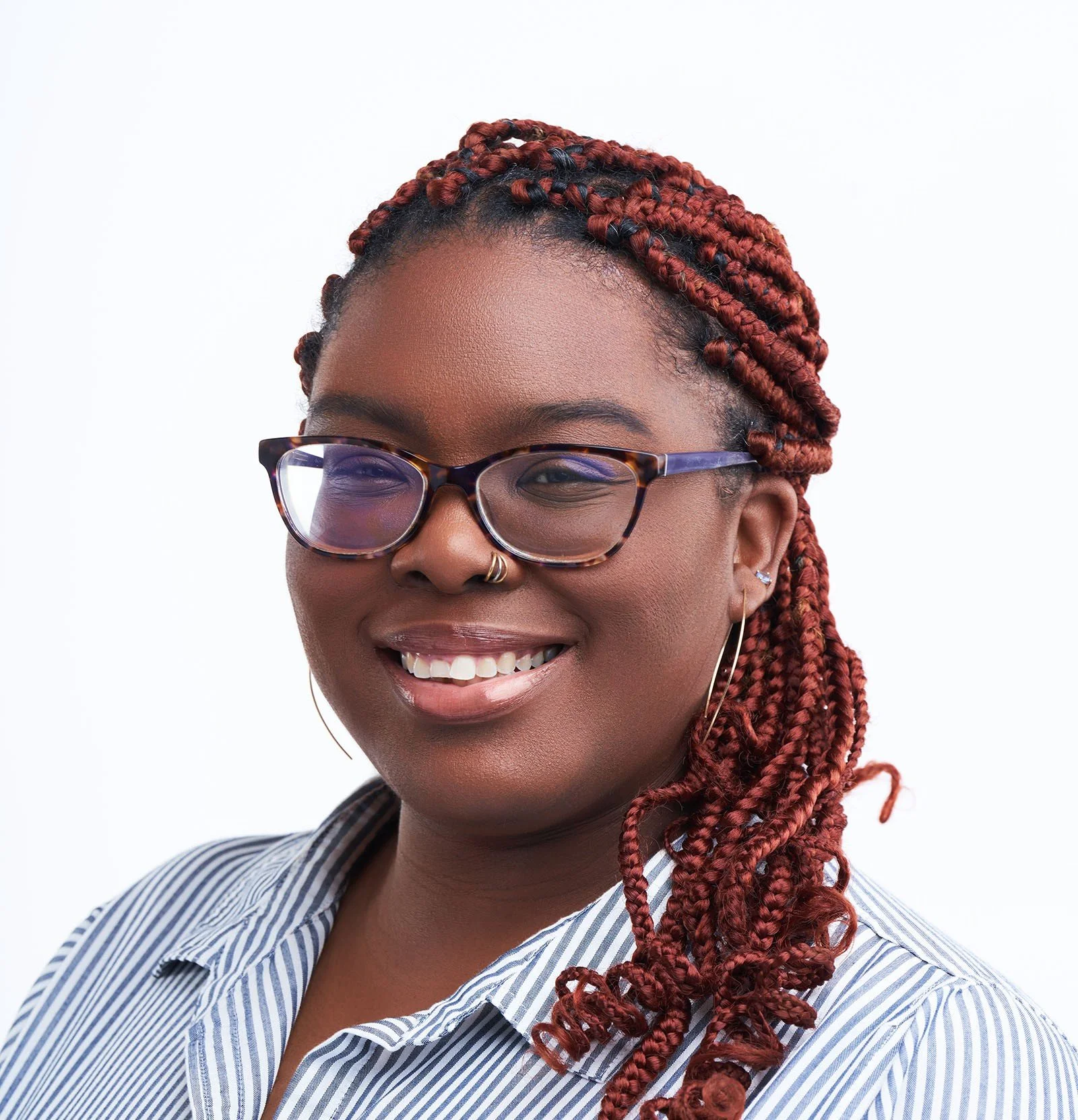 Portrait of a young African American woman smiling, wearing glasses, hoop earrings, a nose ring, and a striped shirt.