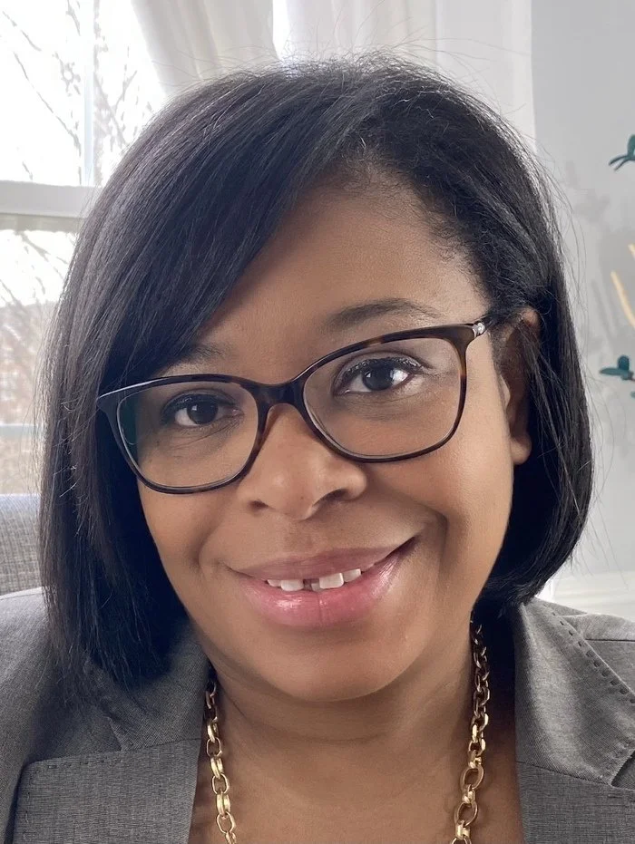 Icon of a person in a minimalist flat design style, with a circular head and rectangular shoulders, in shades of red on a beige background.