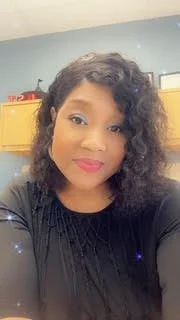 A woman with curly black hair and pink lipstick taking a selfie in a room with blue walls and yellow cabinets.