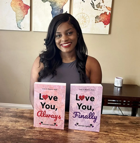 A woman with long dark hair smiling and sitting behind two pink and purple books titled "Love You, Always" and "Love You, Finally" with a map art on the wall behind her.