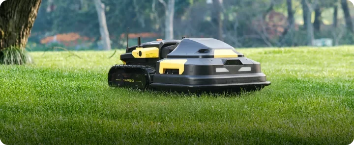 Autonomous robotic lawn mower on a grassy lawn in a park-like setting.