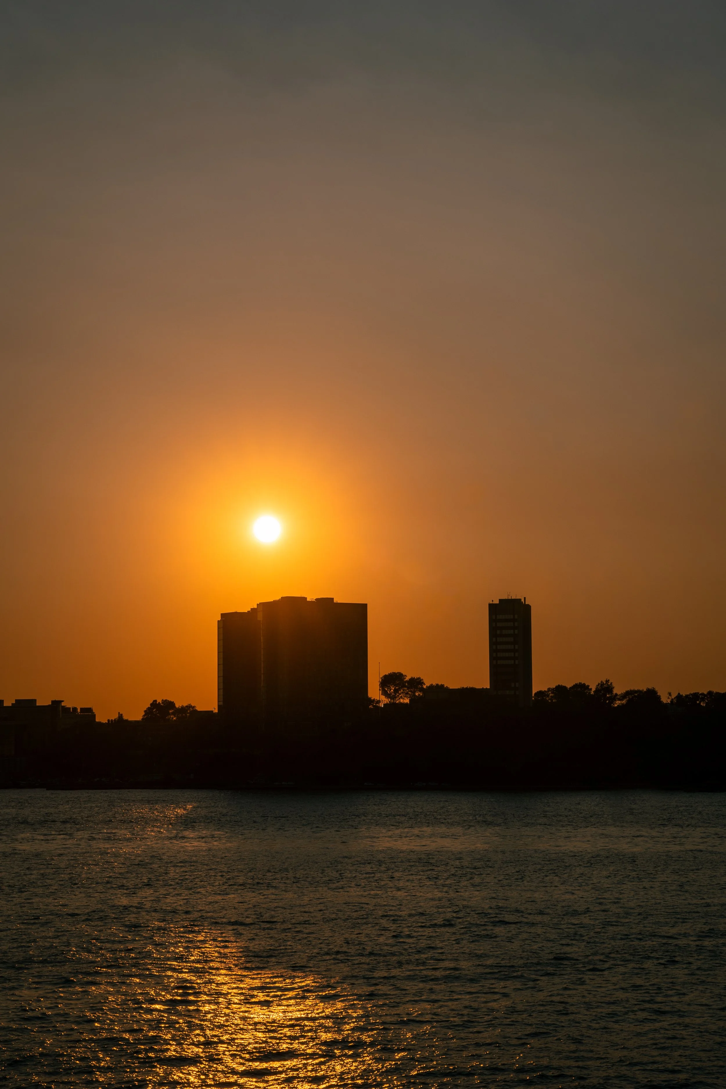 A view of some silhouetted buildings in Hoboken, New Jersey, from the the Pier 57 Rooftop Park. Taken at sunset in 2021.