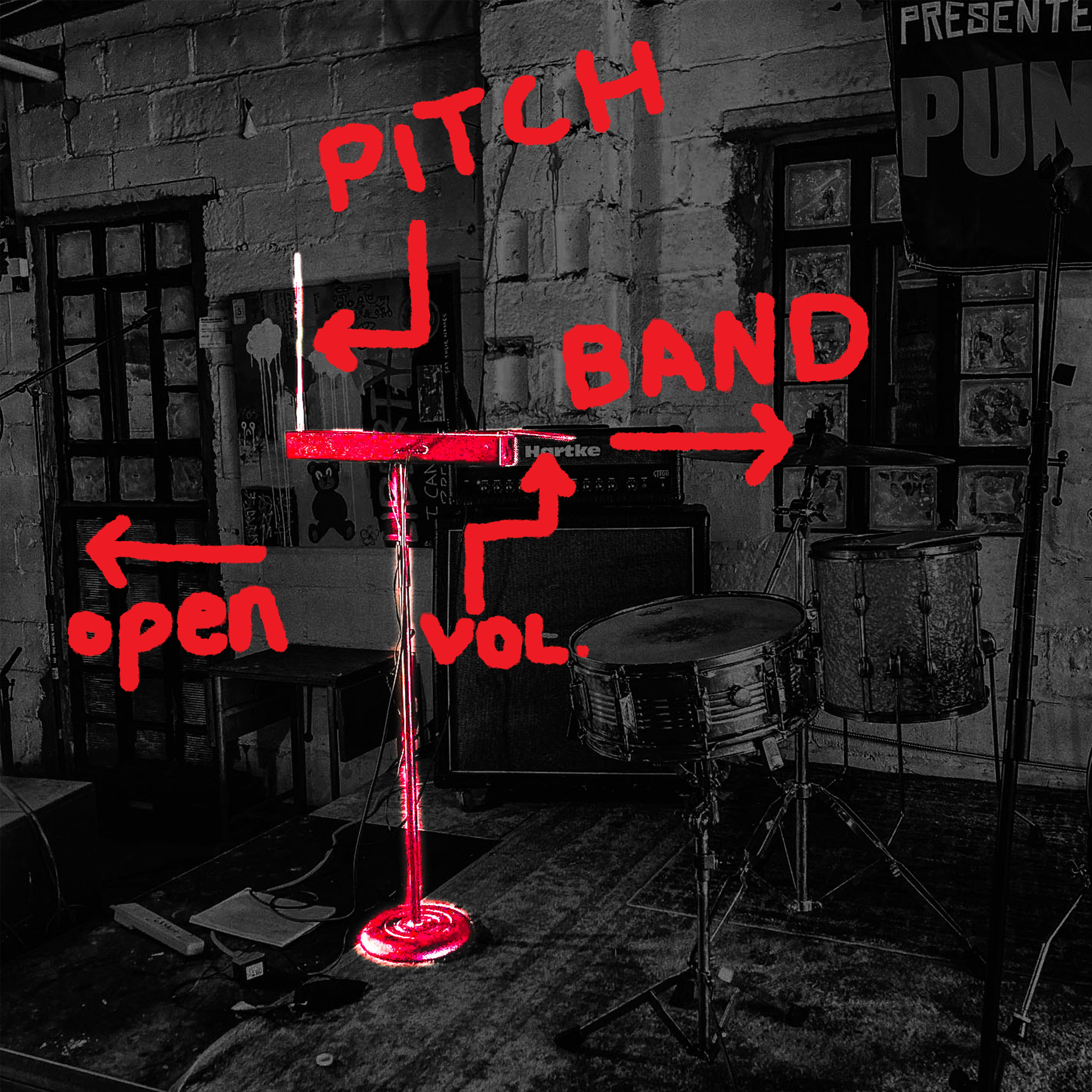 Stage with musical instruments and equipment, including a microphone stand with a red light, drums, and a band setup, in a room with brick walls. Red handwritten labels indicate the microphone is for "PITCH," the drum set with "BAND," a volume control labeled "VOL," and an open microphone or switch labeled "open."