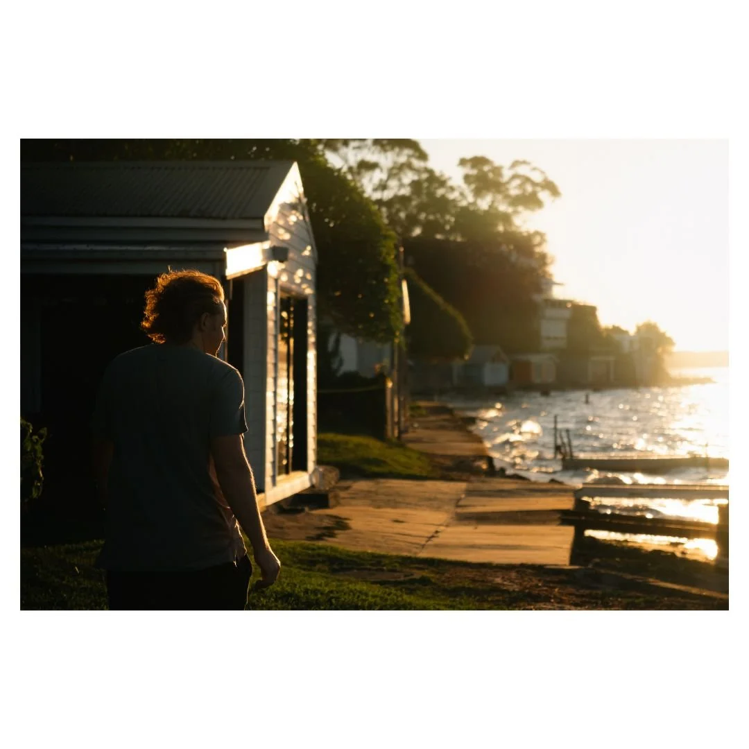 Lifestyle photograph of a person walking by the water at sunset, capturing a coastal Sydney mood.