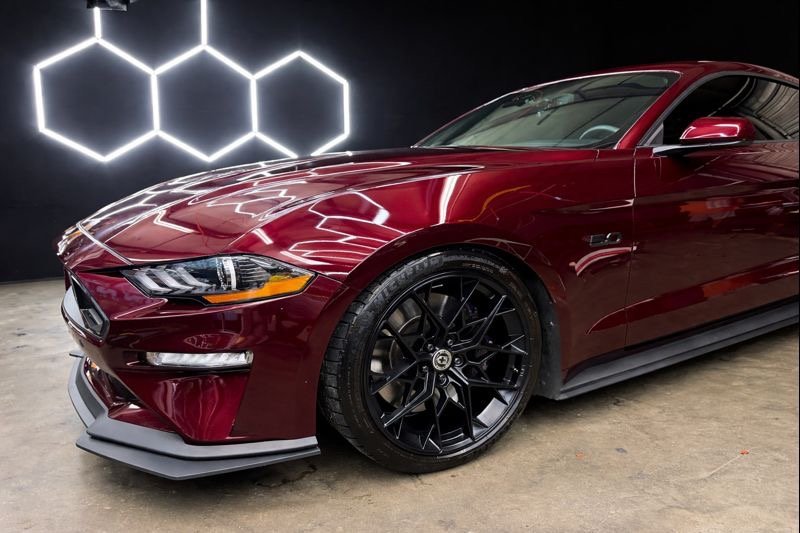 A red sports car with black rims parked indoors with a black wall featuring illuminated hexagon shapes in the background.