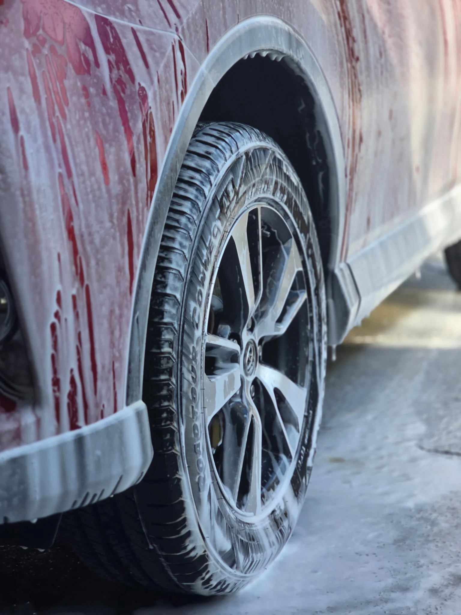 Close-up of a car tire being washed with soap suds on a red vehicle.