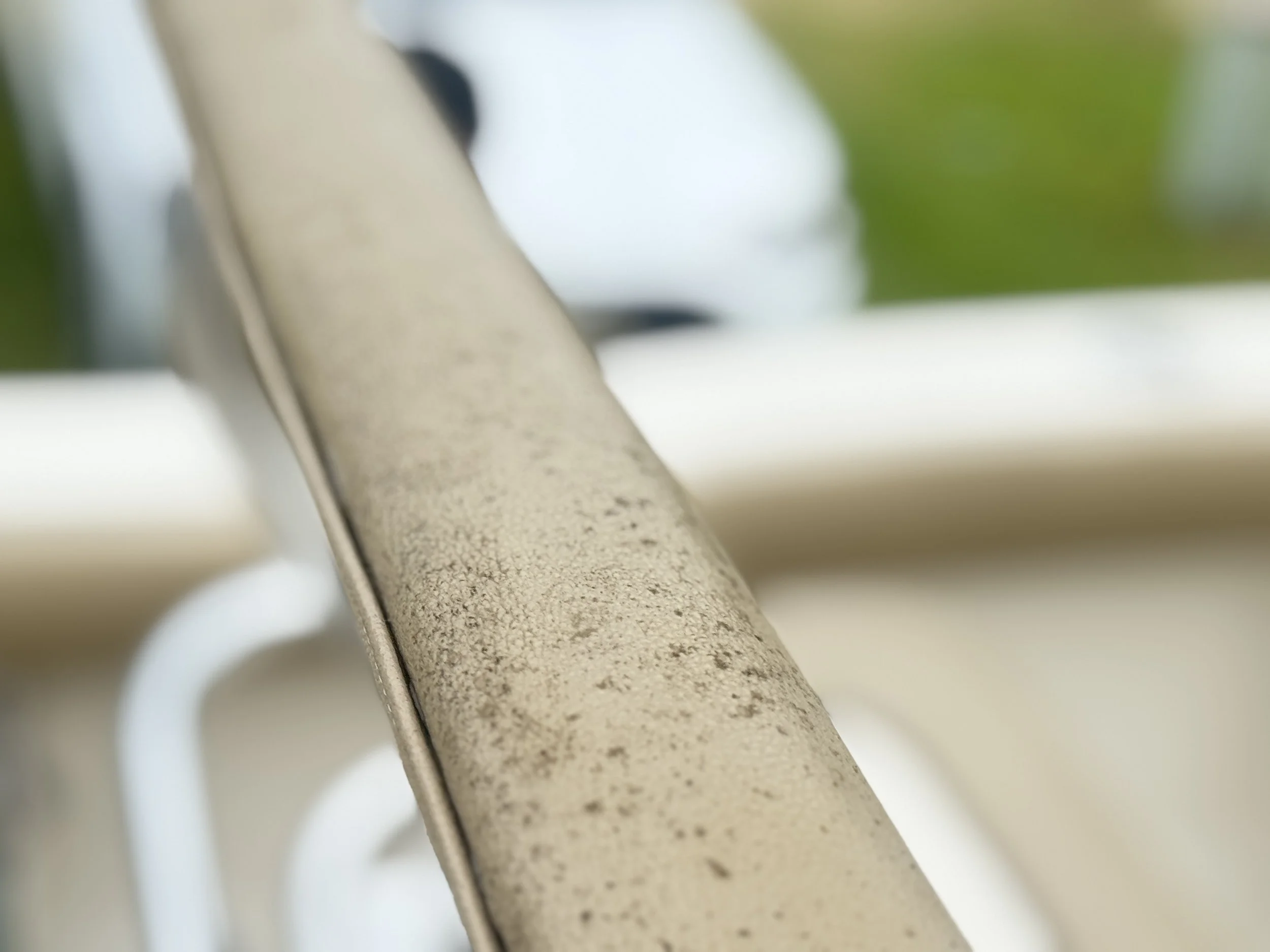 Close-up of a dirty, rusty railing with a blurry background of greenery.