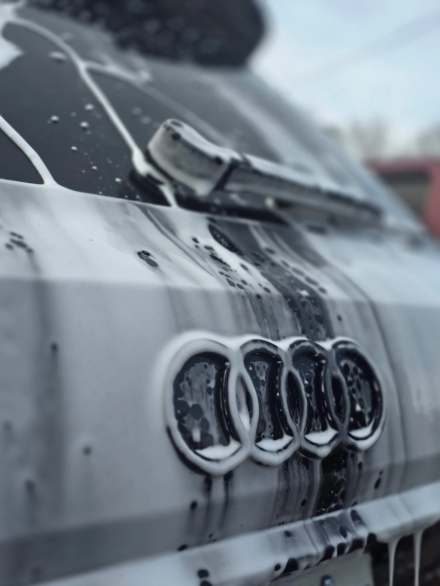Close-up of a silver Audi car with soap suds on the hood and front grille.
