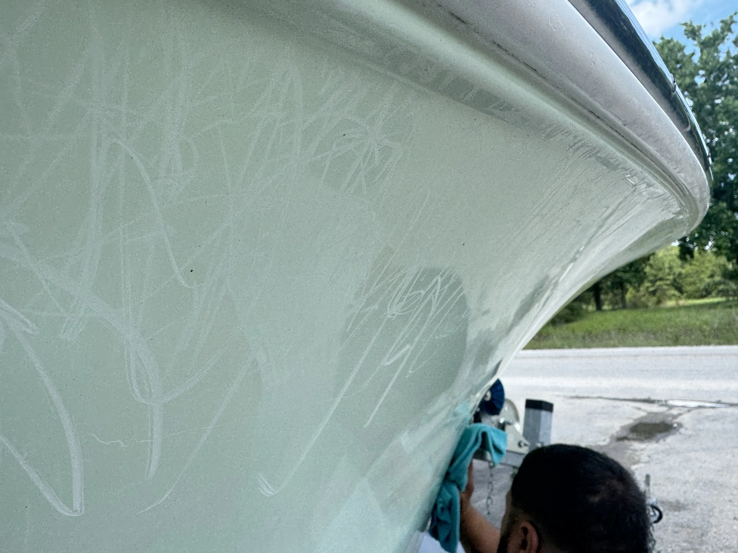 Close-up of a boat's side with scratches being buffed out, with a person cleaning or polishing the boat's surface on the right side.