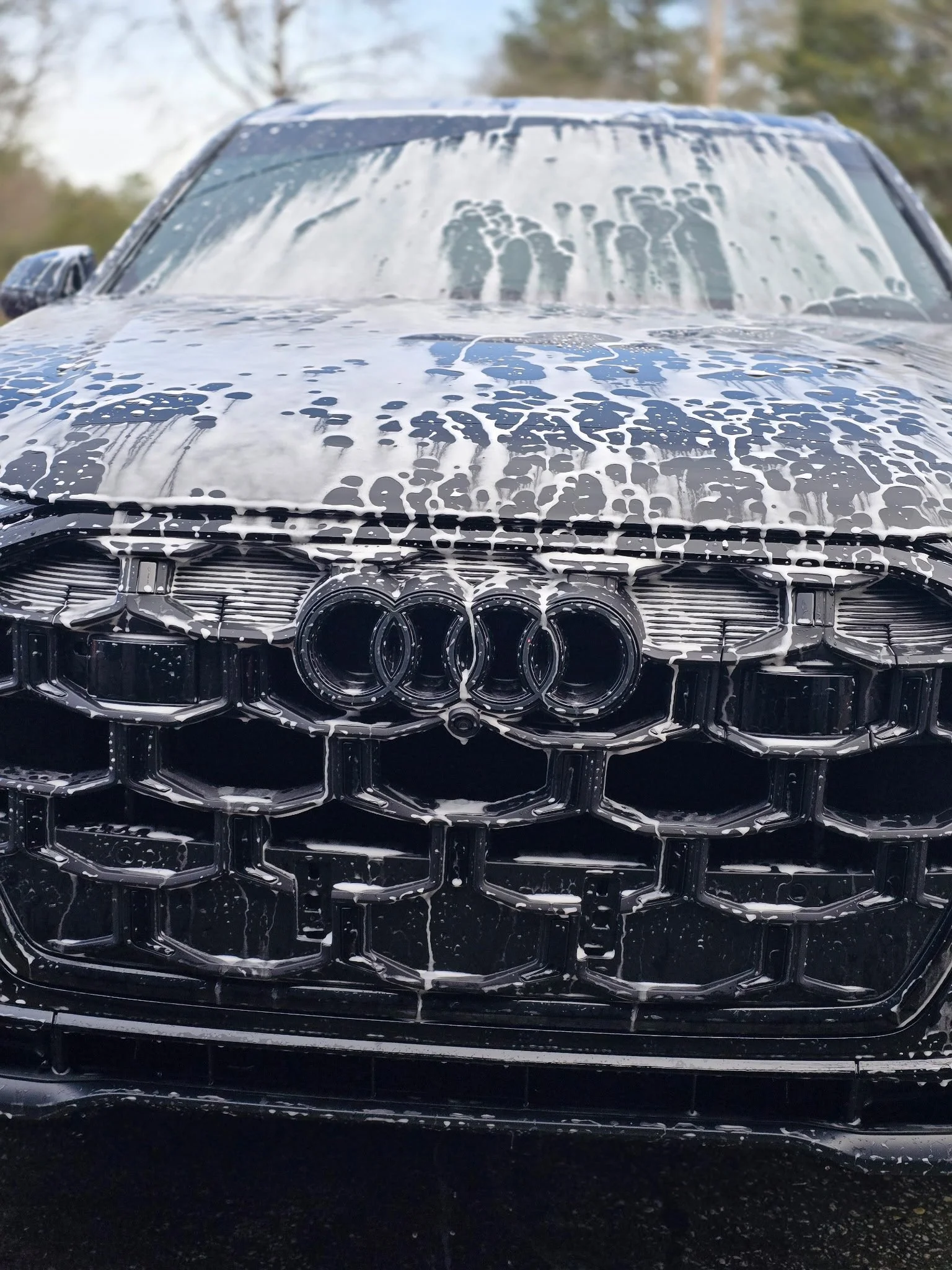 A black Audi car being washed with soap suds on the hood and windshield.