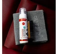 A bottle of disinfectant spray and a rectangular black box placed on a gray textured cloth. The background includes a red surface.