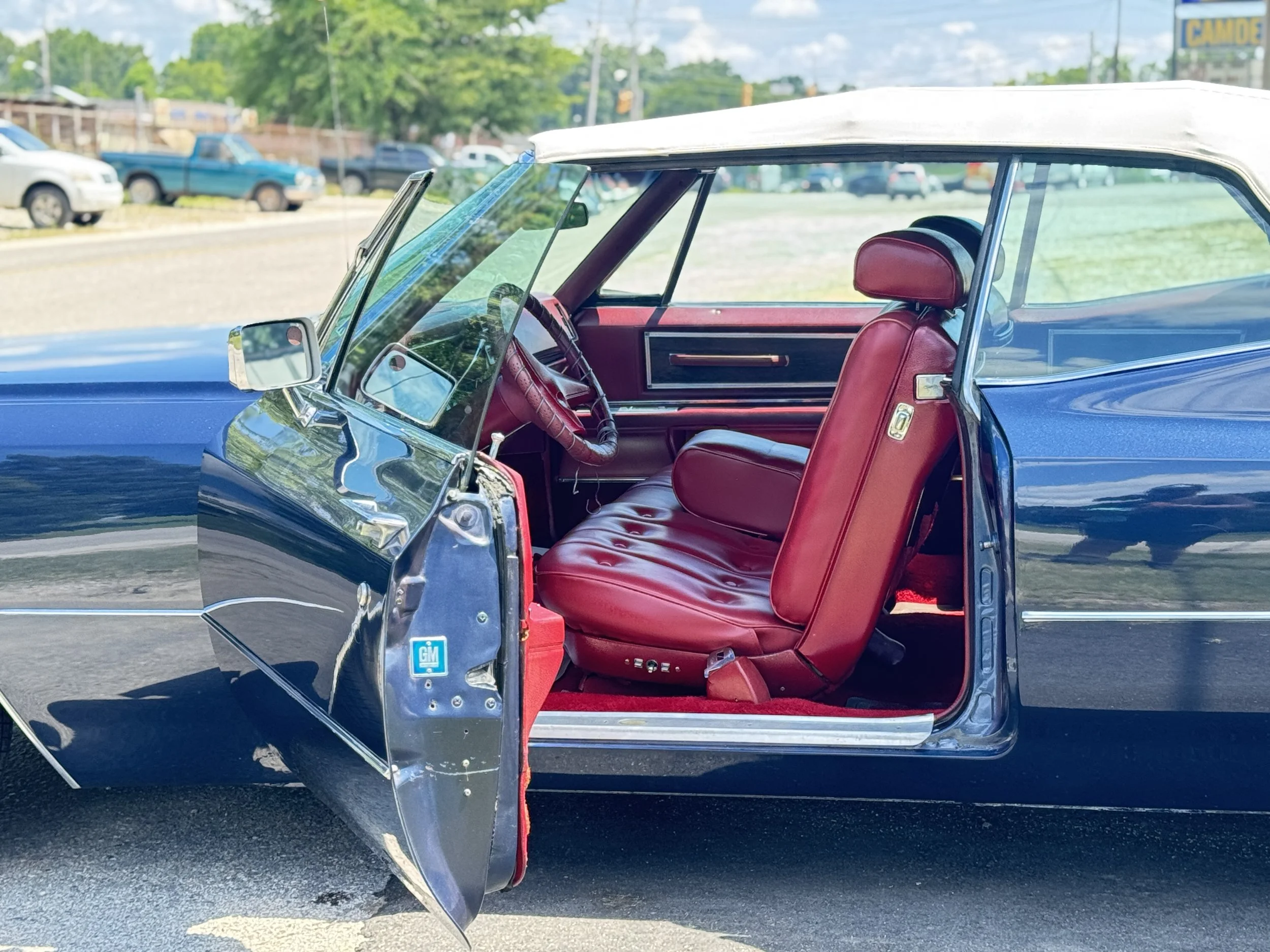 Interior of a vintage blue and white convertible car with red leather seats, parked outdoors with other vehicles and greenery in the background. ceramic g wash
