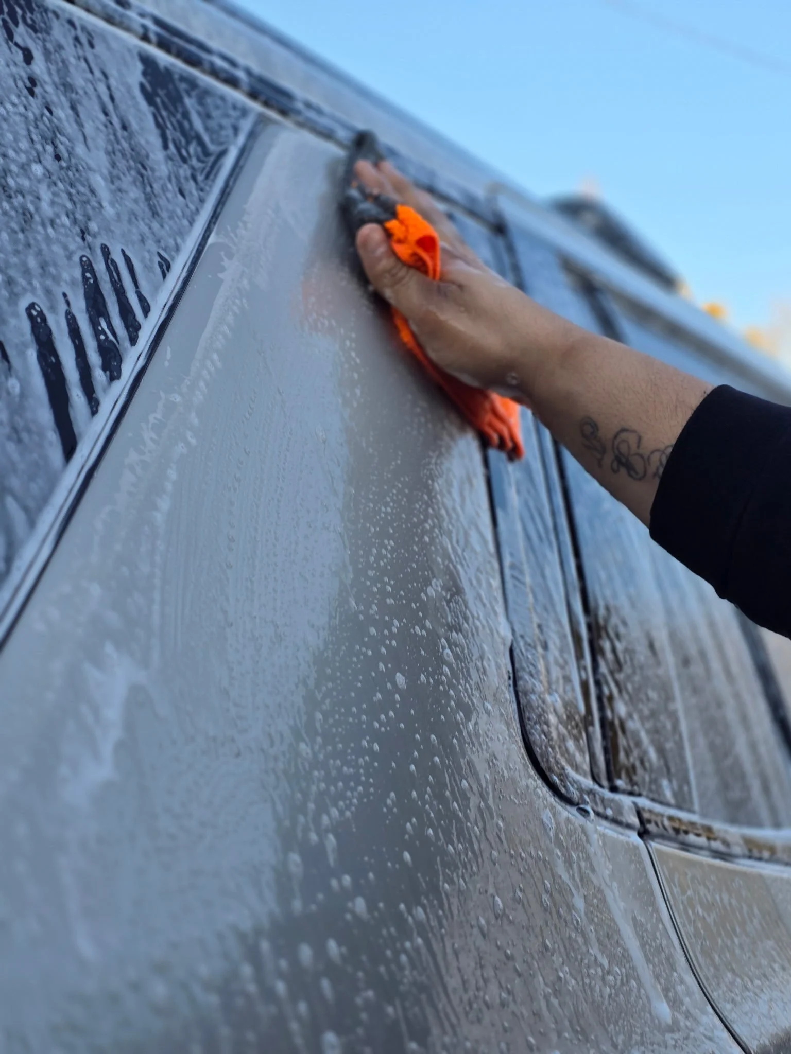Person washing a car with an orange cloth in outdoor setting.