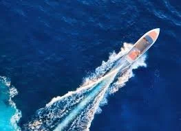 A speedboat speeding across the ocean, creating a large wake and spray.