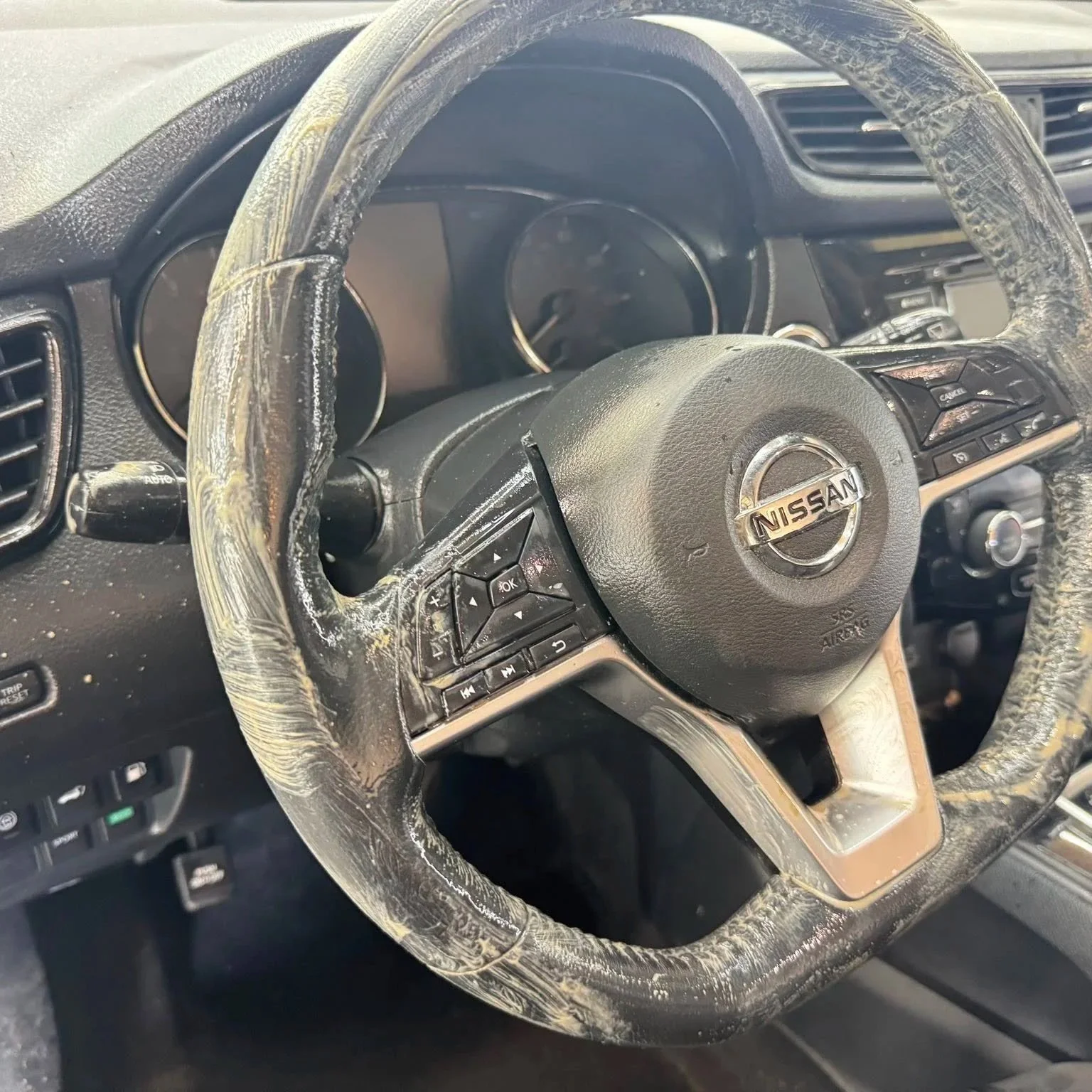 Nissan steering wheel with damaged and worn black leather cover, showing signs of extensive wear and tear, inside a car with a black interior.