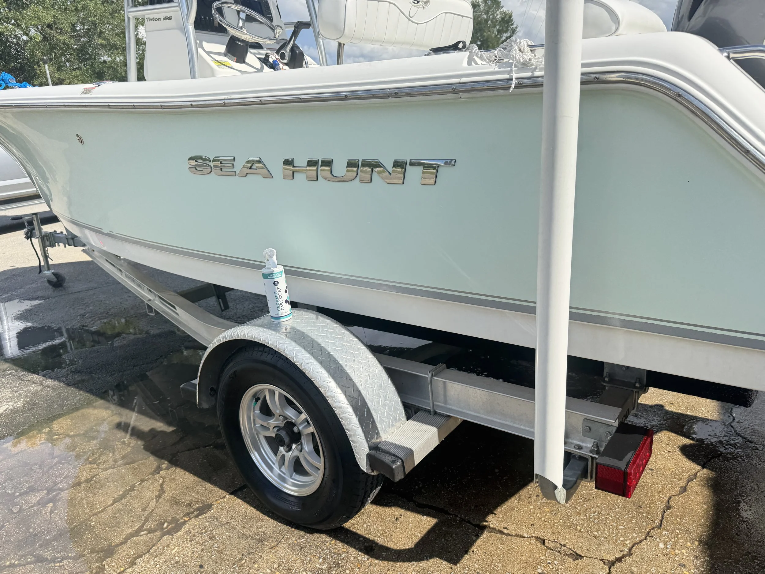 A light blue Sea Hunt boat on a trailer at a boat dealership, with a hand sanitizer bottle placed on the trailer wheel.