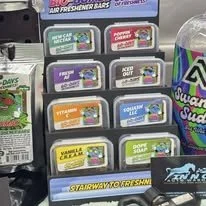 Display of various flavor Air Delight insect repellent sticks on a store shelf, with a large container of Swatters Foam Scourer in the background.