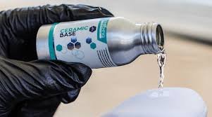 A hand wearing a black glove pouring ceramic coating from a bottle onto a surface.