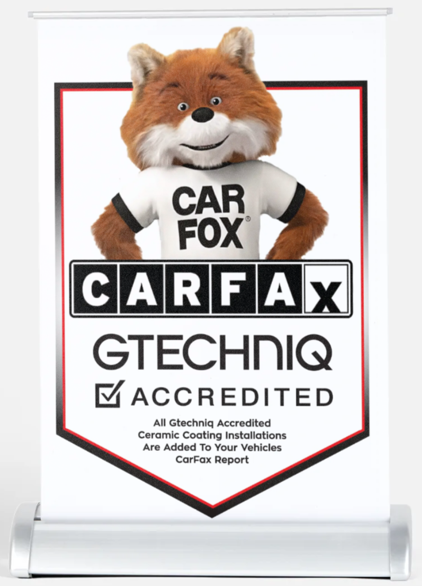A vertical banner featuring the Car Fox mascot, a cheerful fox wearing a white t-shirt with "CAR FOX" written on it. The banner promotes Carfax, highlighting that the service is Gtechniq accredited for ceramic coating installations on vehicles. The bottom includes details about accreditation and services offered.