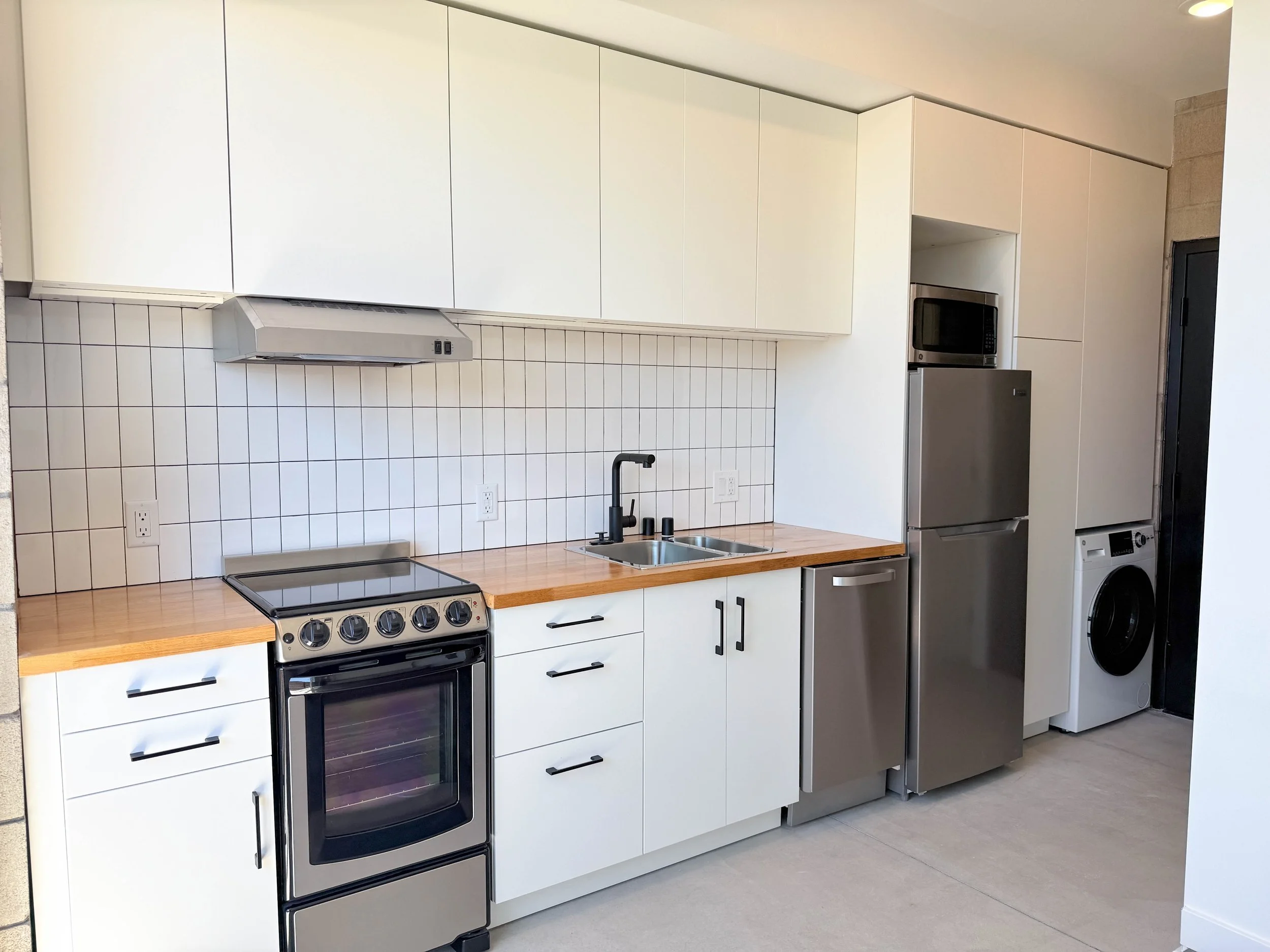 Modern white bathroom with bathtub, toilet, washing machine, sink, and mirror.