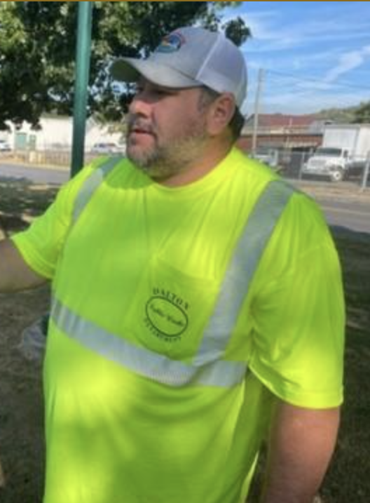Man wearing a white cap and bright yellow safety shirt with reflective stripes, outdoors on a sunny day.