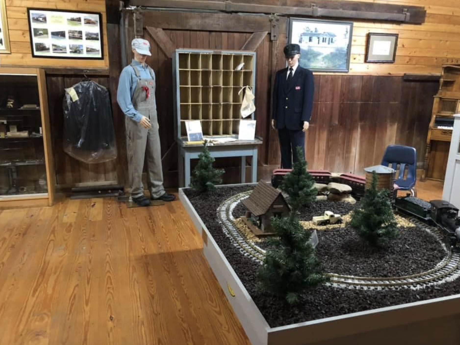 A museum exhibit featuring vintage train conductors and a miniature train set with trees and a small building.