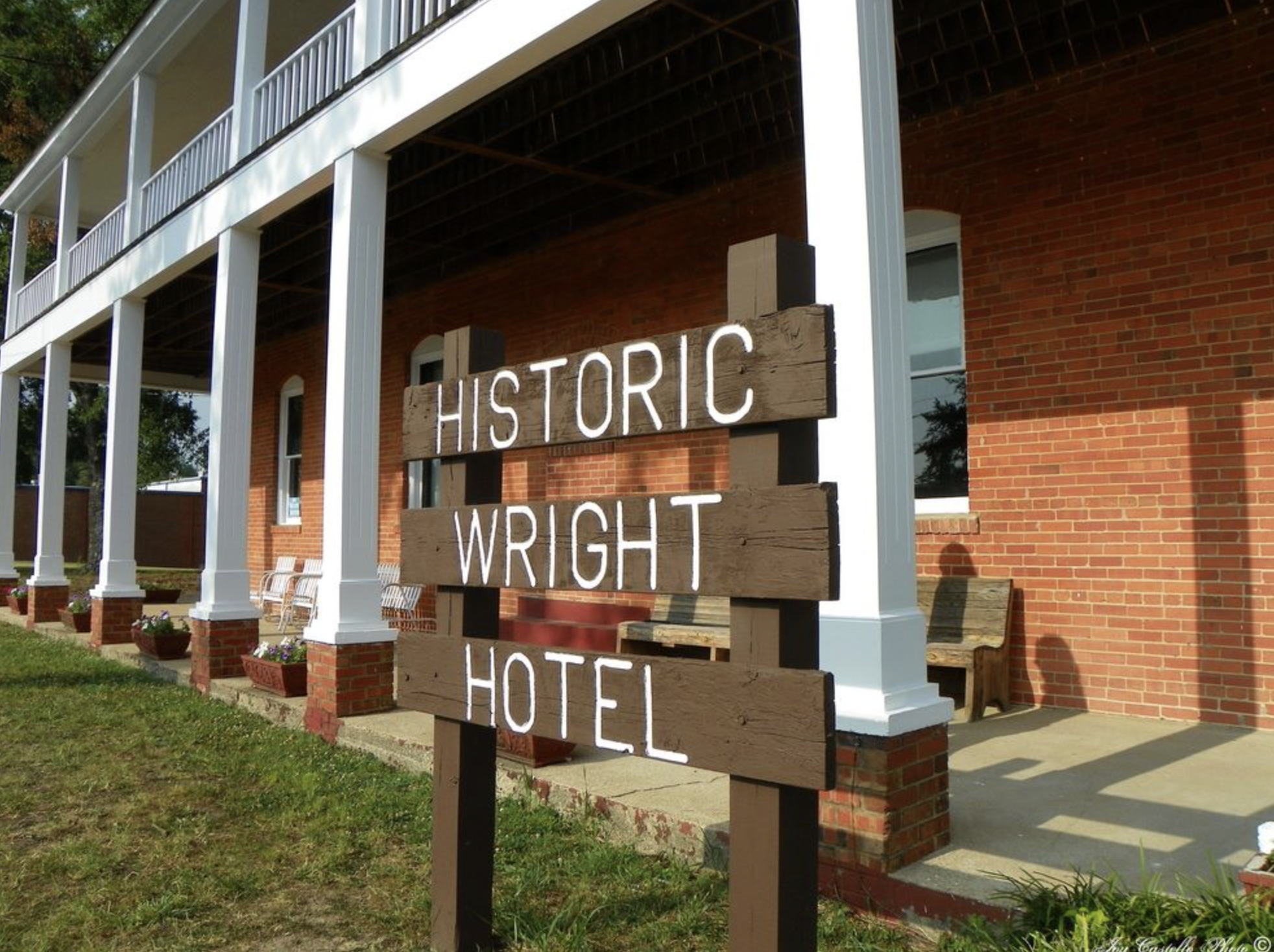 A sign made of wooden planks with white painted letters reading 'HISTORIC WRIGHT HOTEL' in front of a brick building with white columns.