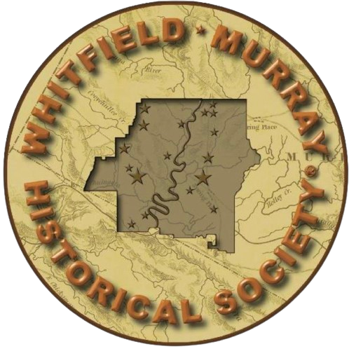 A circular emblem with a map outline of Washington State in the center, featuring stars marking specific locations. Encircling the map are the words 'Whitefield Murrah Historic Society' in 3D gold letters.