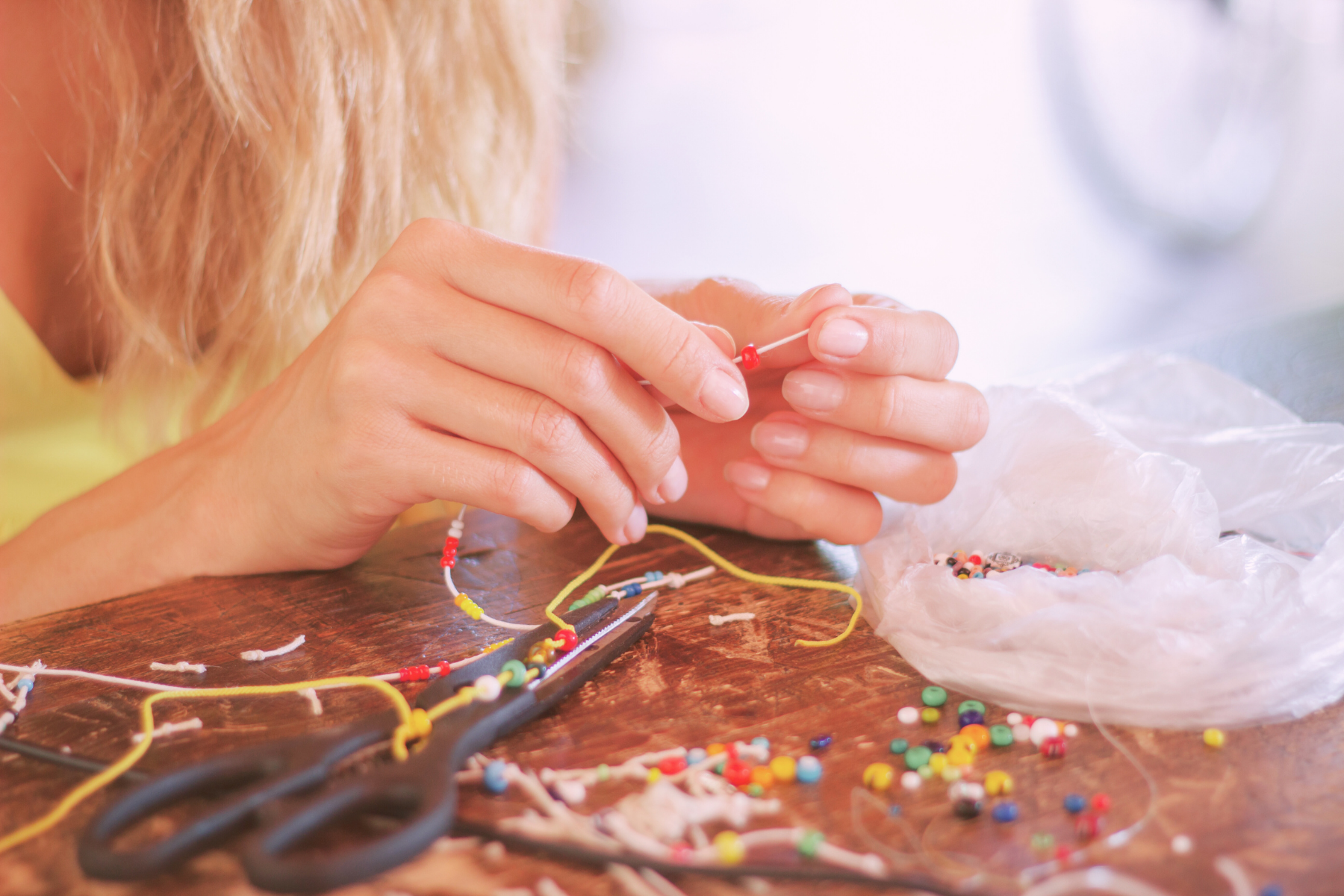 a pair of hands threading a bead next to a bag of assorted beads
