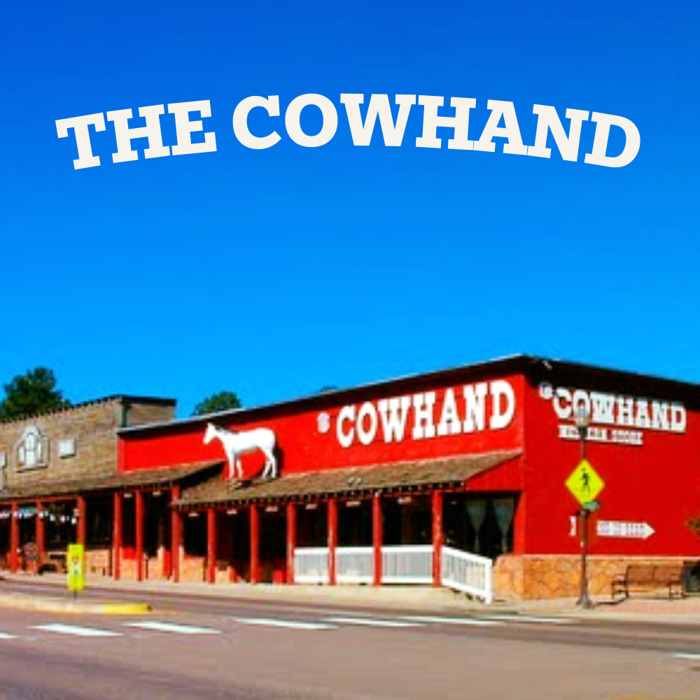 Red building with a white goat sculpture on the roof, and the words 'THE COWHAND' in large white letters on top, with a yellow pedestrian crossing sign in front.