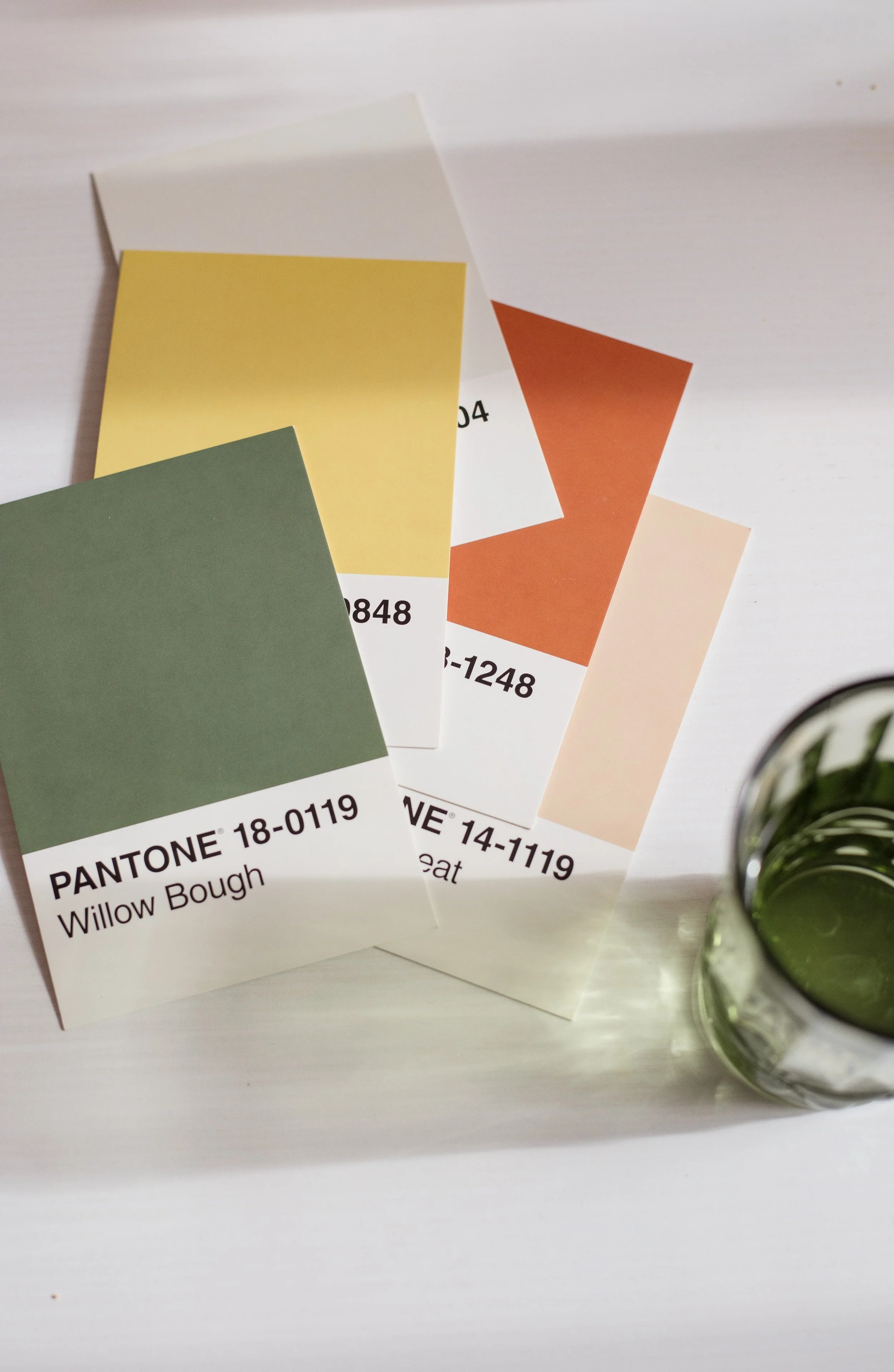 Color swatches labeled with Pantone codes, including Willow Bough, with a glass of water on a white surface.