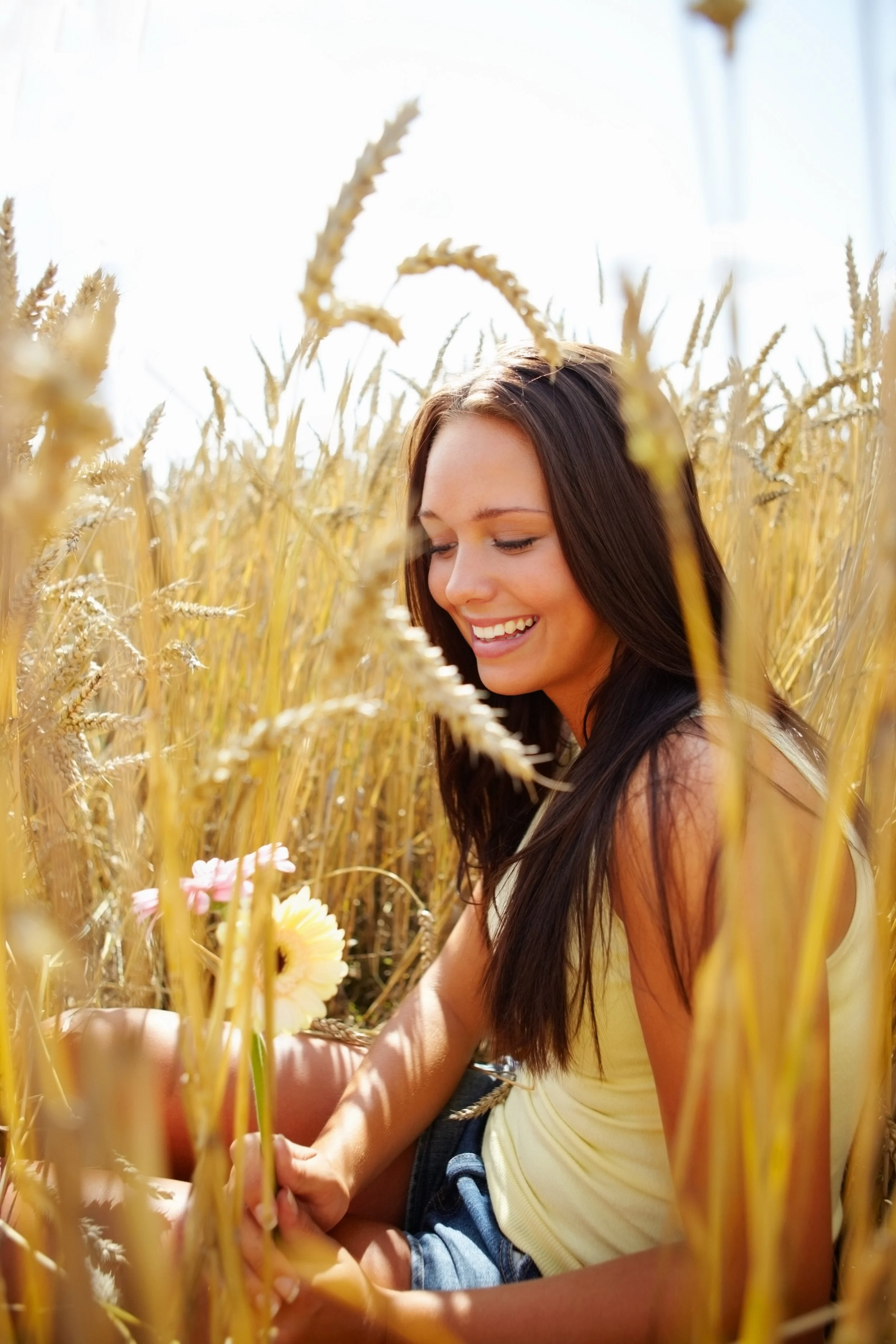 A young woman with long brown hair sitting in a wheat field , feeling the nature