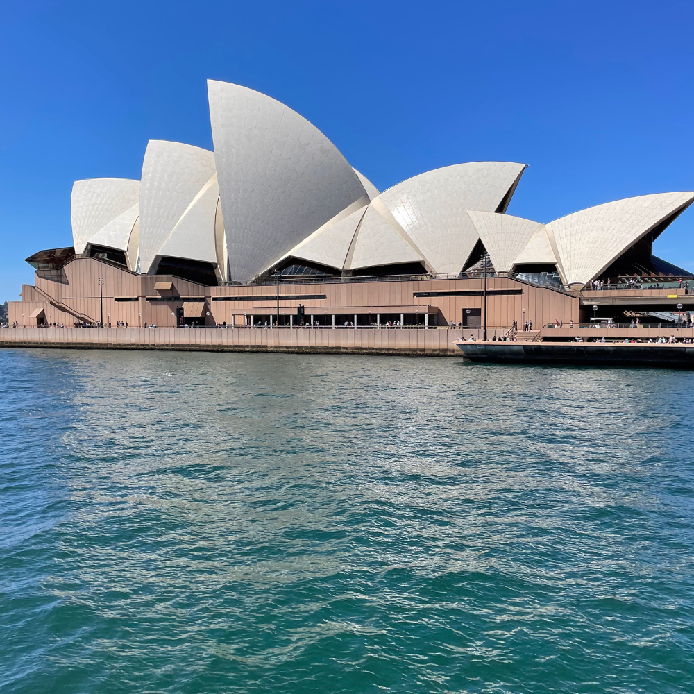 Sydney Opera House with white sail-like structures on the waterfront against a clear blue sky.